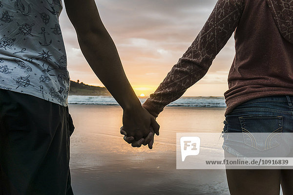Paar steht Hand in Hand am Strand mit Blick auf den Sonnenuntergang  Teilansicht