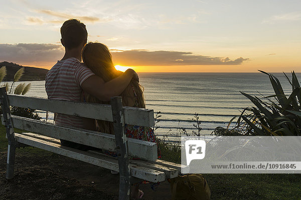 Verliebtes Paar sitzt auf der Bank und schaut auf den Sonnenuntergang.