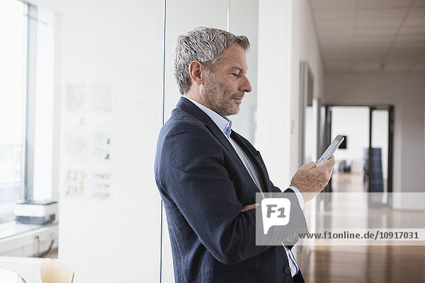 Erfolgreicher Geschäftsmann  der in seinem Büro ein digitales Tablett hält.