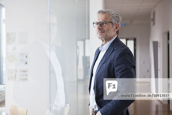 Successful businessman standing in his office looking out of window