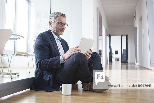 Successful businessman sitting on floor  using digital tablet in his office