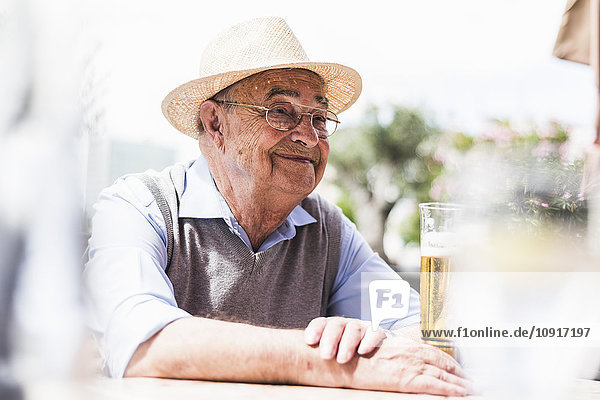 Porträt eines glücklichen älteren Mannes  der in einem Straßencafé ein Glas Bier trinkt.
