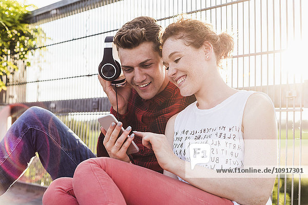 Lächelndes junges Paar am Zaun mit Kopfhörer und Smartphone