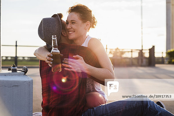 Glückliches junges Paar mit Bierflaschenumarmung bei Sonnenuntergang