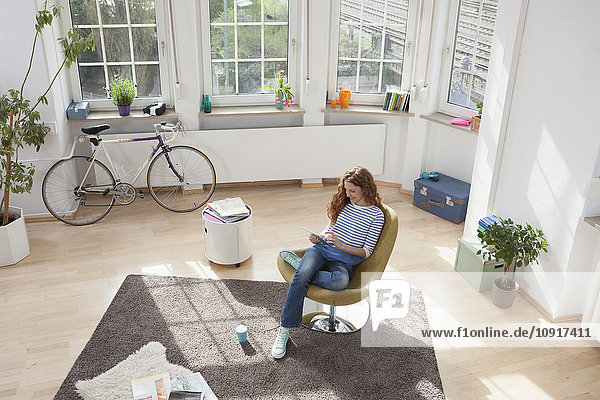 Frau zu Hause im Sessel sitzend mit digitalem Tablett