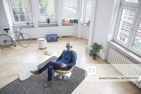Relaxed mature man at home sitting in chair listening to music