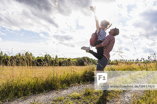 Happy young man lifting up girlfriend on field path