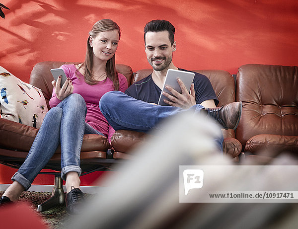 Ein junger Geschäftsmann und eine junge Frau sitzen auf einer alten Couch mit digitalen Geräten.