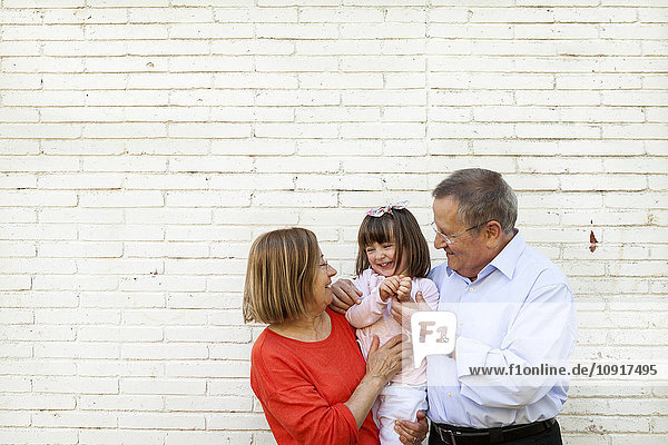 Großeltern mit ihrer Enkelin vor weißer Backsteinmauer