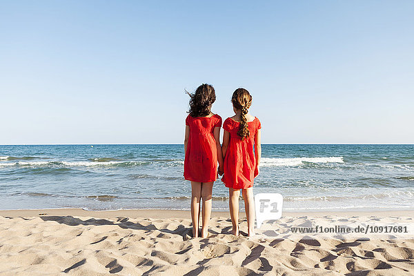 Rückansicht von zwei kleinen Schwestern am Strand mit Blick auf das Meer