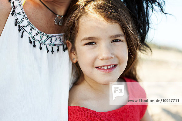 Porträt eines lächelnden kleinen Mädchens neben ihrer Mutter am Strand