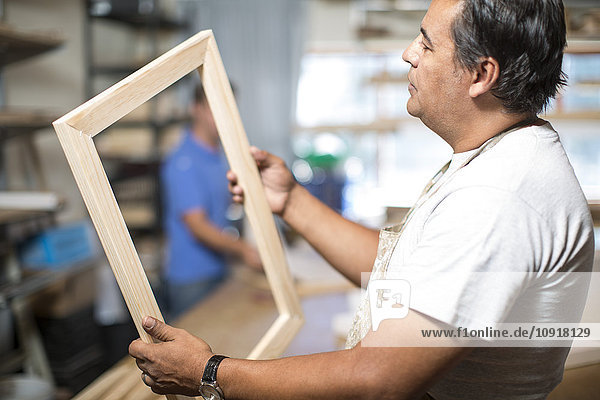Mann betrachtet Holzrahmen für die Leinwandvorbereitung in der Werkstatt