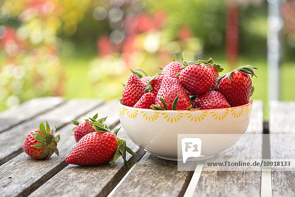 Schale mit Erdbeeren auf Gartentisch aus Holz