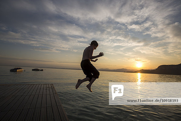 Italy  Veneto  Bardolino  Lake Garda  boy jumping into the water at sunset