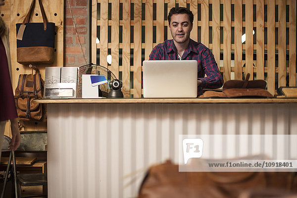 Mann mit Laptop am Ladentisch