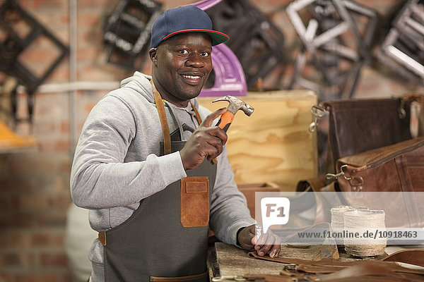 Portrait of smiling man working with hammer in leather workshop
