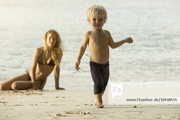 Thailand  glücklicher Junge am Strand mit Mutter im Hintergrund