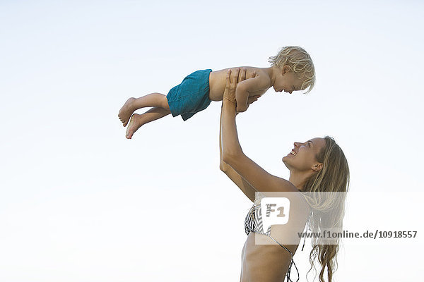 Glückliche Mutter im Bikini hebt ihren Sohn hoch