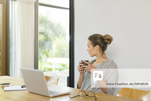 Frau am Tisch mit Tasse Kaffee und Laptop