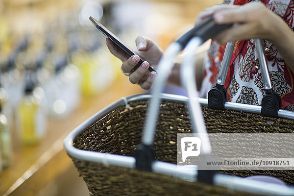 Close-up of woman holding shopping basket and cell phone