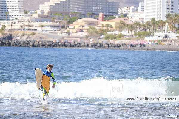 Spanien  Teneriffa  Junge mit Surfbrett im Meer