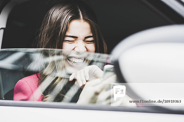 Brunette woman sitting in car laughing about text messages