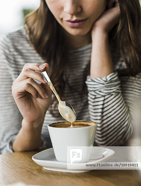 Junge Frau trinkt Cappuccino  Löffelchen Milchschaum