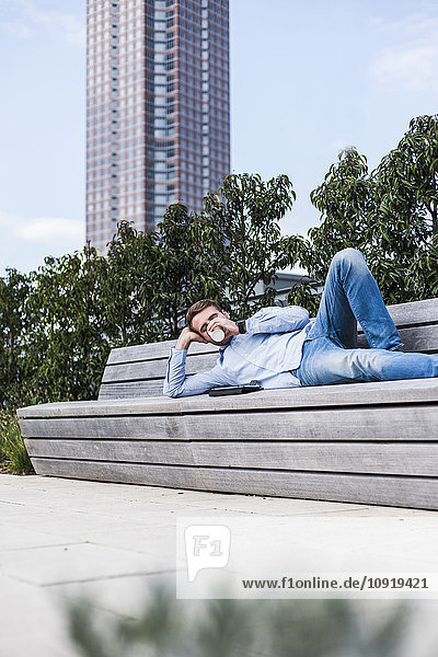 Junger Mann auf der Bank liegend mit digitalem Tablett