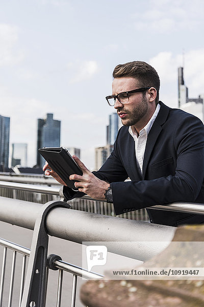 Junger Geschäftsmann mit digitalem Tablett auf der Brücke stehend
