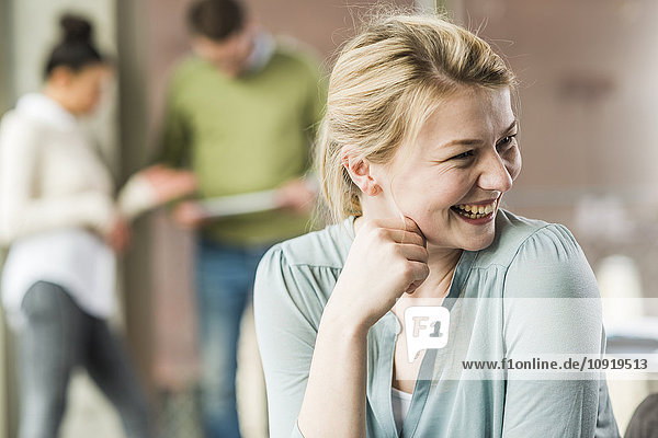 Happy young woman in office with colleagues in background