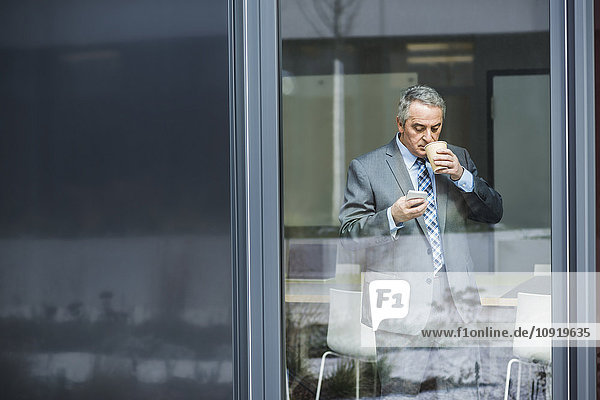 Senior businessman holding coffee to go looking on cell phone