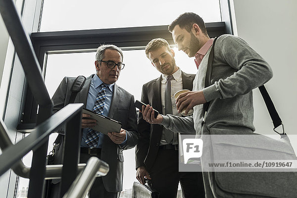 Three businessmen with digital tablet and cell phone in staircase