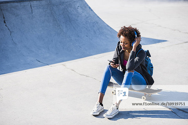 Junge Frau sitzt auf dem Skateboard und hört Musik.