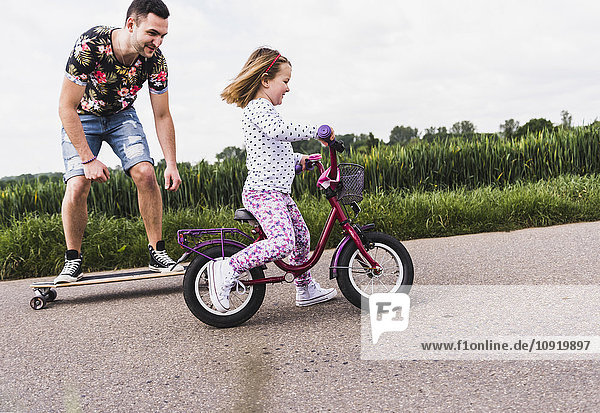 Father on skateboard accompanying daughter on bicycle
