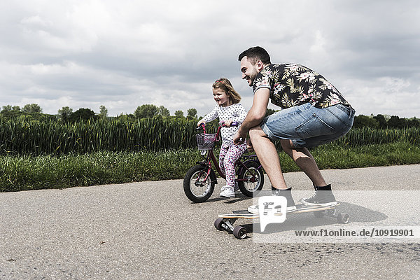 Father on skateboard accompanying daughter on bicycle