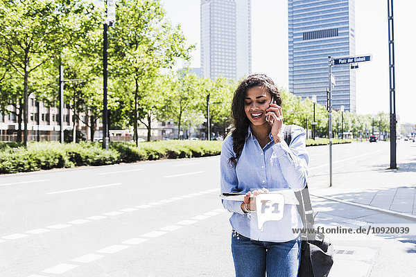 Lächelnde junge Frau am Handy mit Blick auf Dokument im Freien