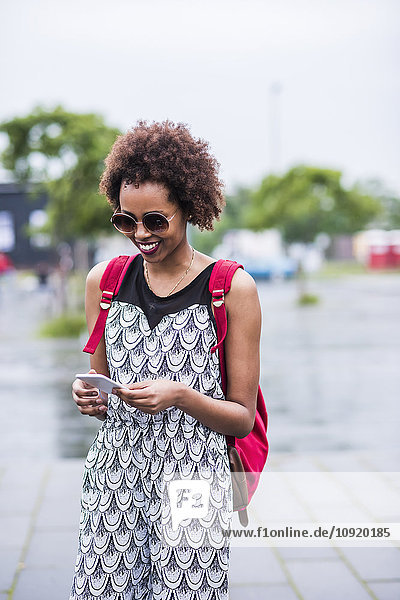 Porträt einer lächelnden jungen Frau  die ihr Smartphone ansieht.