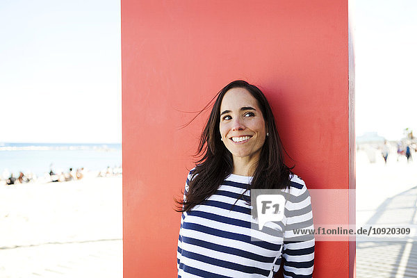 Spanien,  Barcelona,  Porträt einer Frau mit gestreiftem Pullover,  die sich gegen das rote Paneel lehnt.