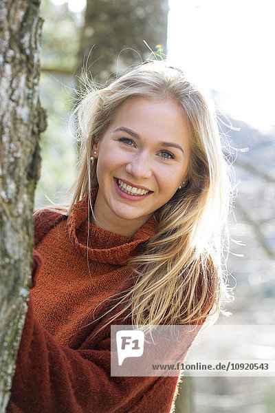 Portrait of happy teenage girl besides tree trunk