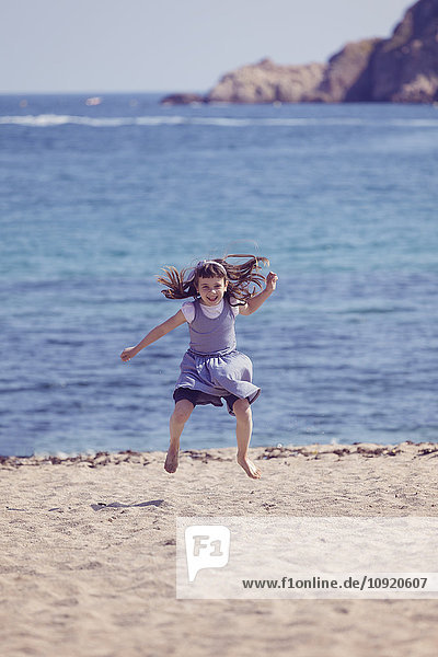 Spanien  glückliches kleines Mädchen  das am Strand in die Luft springt.