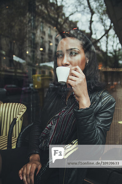 Porträt einer jungen Frau  die hinter der Fensterscheibe eines Cafés sitzt und Kaffee trinkt.