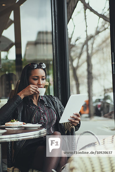 Porträt einer jungen Frau  die in einem Café sitzt und beim Kaffeetrinken auf eine digitale Tafel schaut.