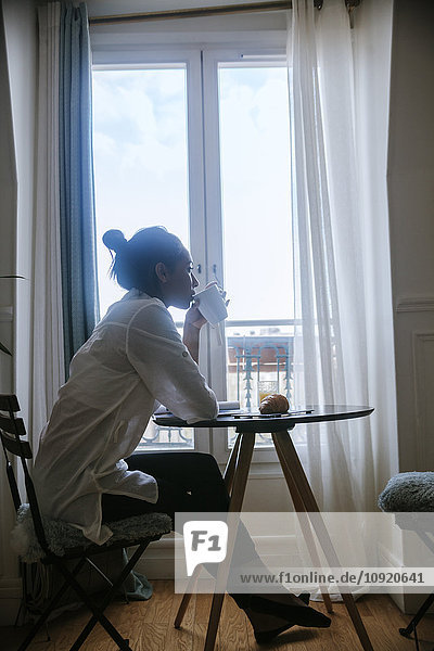 Junge Frau sitzt am Frühstückstisch und trinkt Kaffee.
