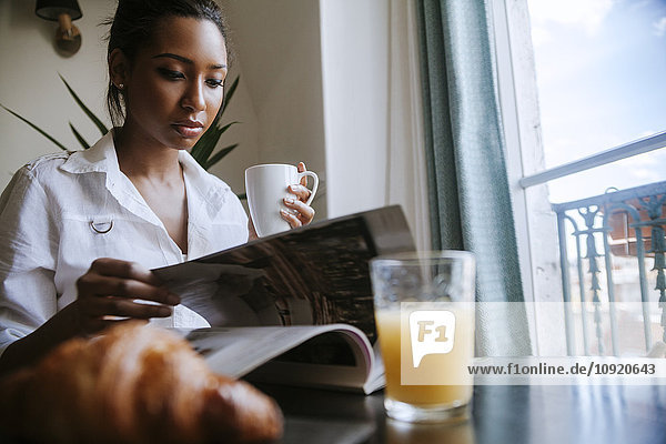 Porträt einer jungen Frau beim Lesen am Frühstückstisch