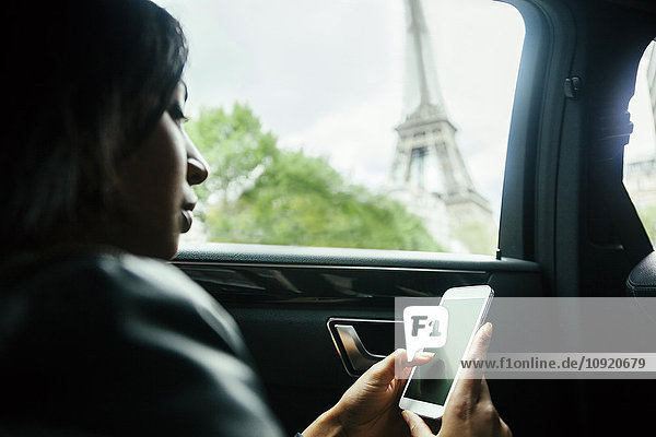 Frankreich  Paris  junge Frau sitzt im Auto und schaut auf ihr Smartphone.