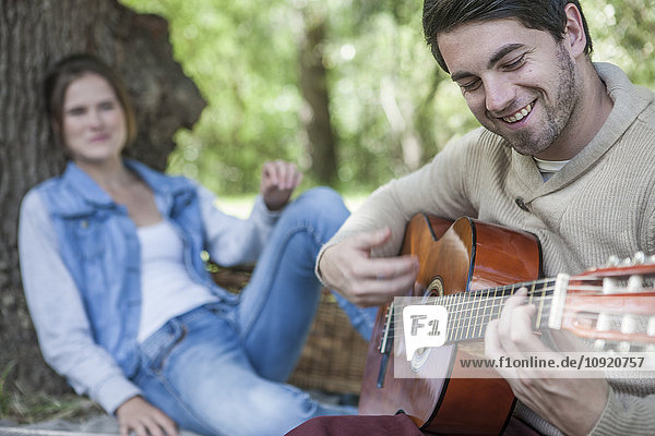 Young couple having a picnic with man playing guitar