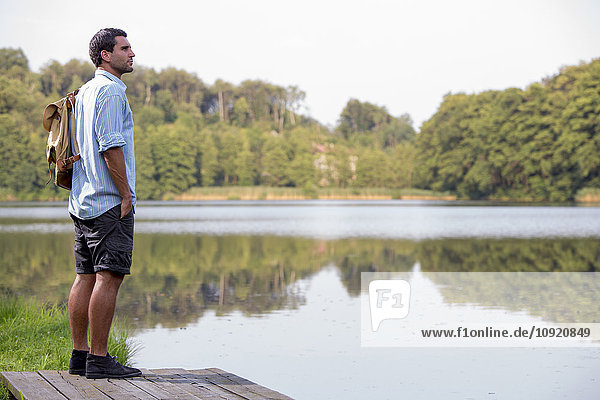 Junger Mann steht auf einem Steg am See und schaut in die Ferne.