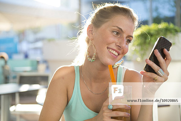Blonde junge Frau im Outdoor-Café mit Blick auf ihr Smartphone