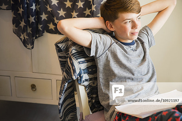 Selbstbewusster Junge macht Hausaufgaben mit den Händen hinter dem Kopf