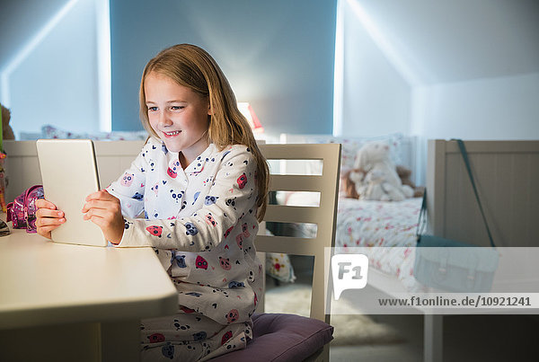 Mädchen im Pyjama mit digitalem Tablett am Schreibtisch im Schlafzimmer